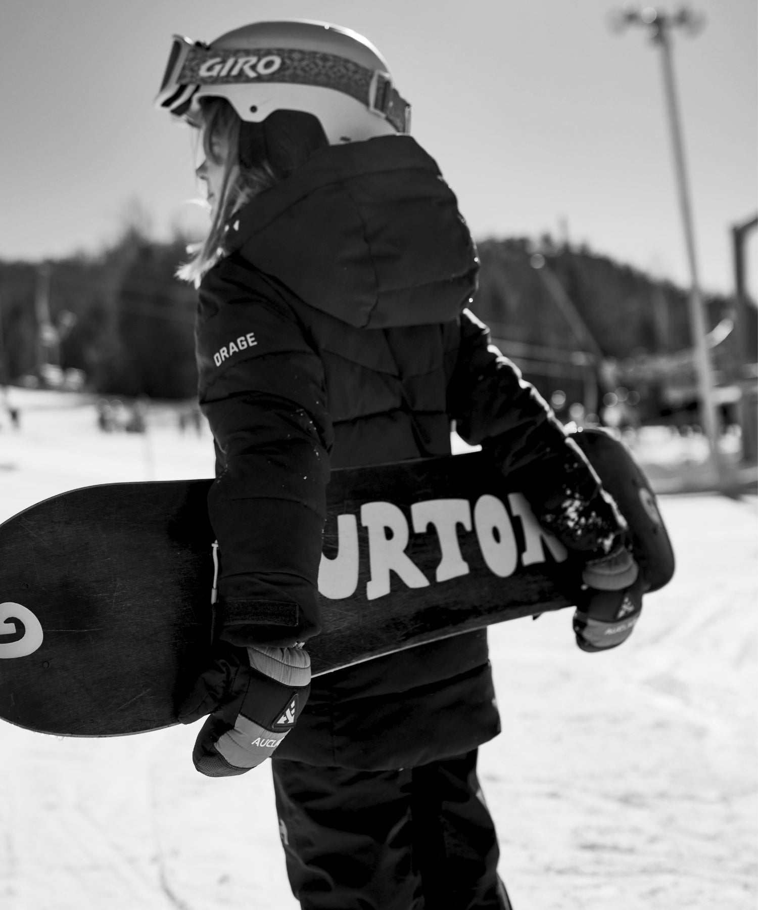 Young snowboarder carrying a snowboard and wearing Auclair gloves, geared up for a day on the slopes.