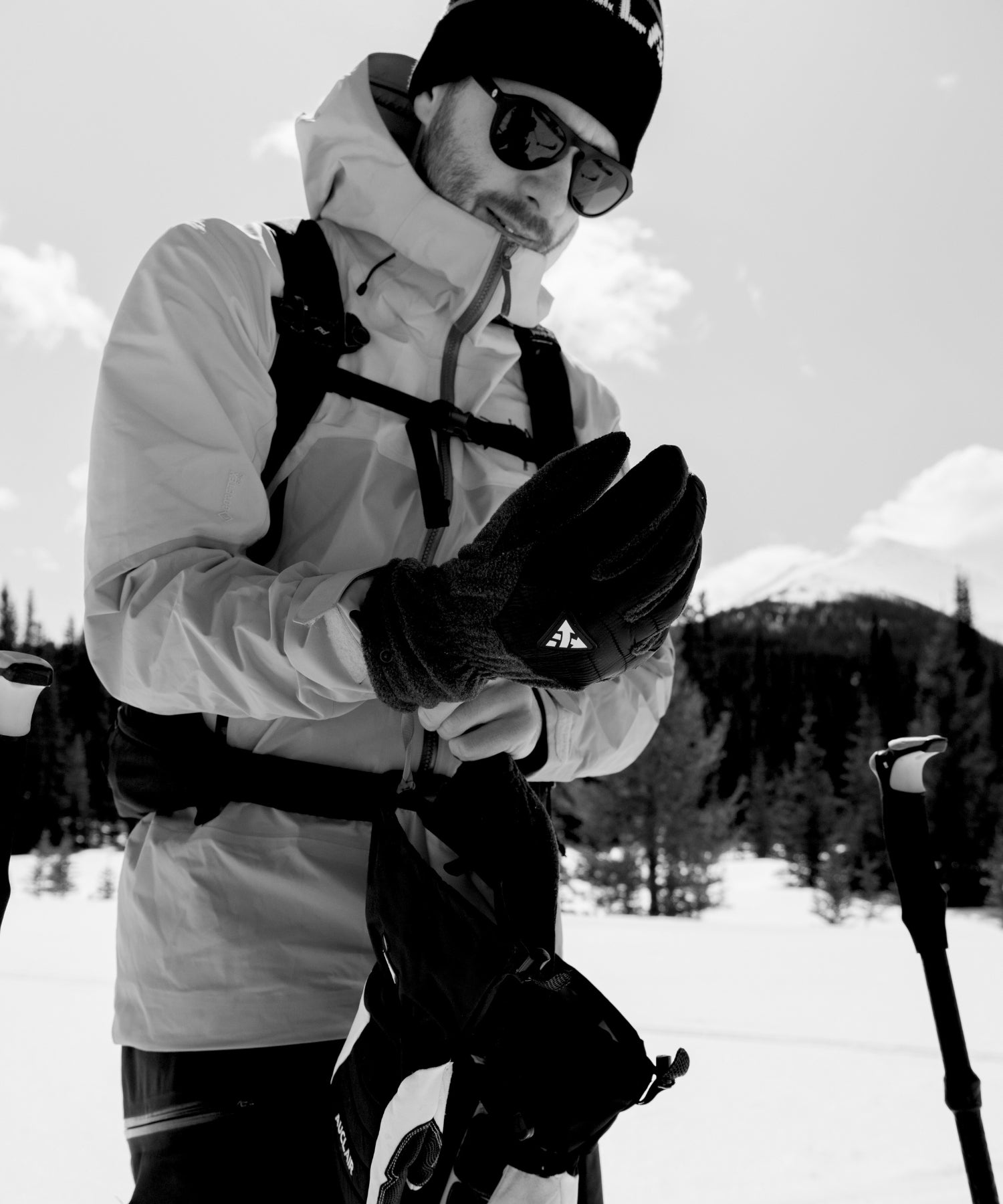 Man adjusting Auclair winter gloves on a snowy mountain, showcasing the Auclair men's collection.