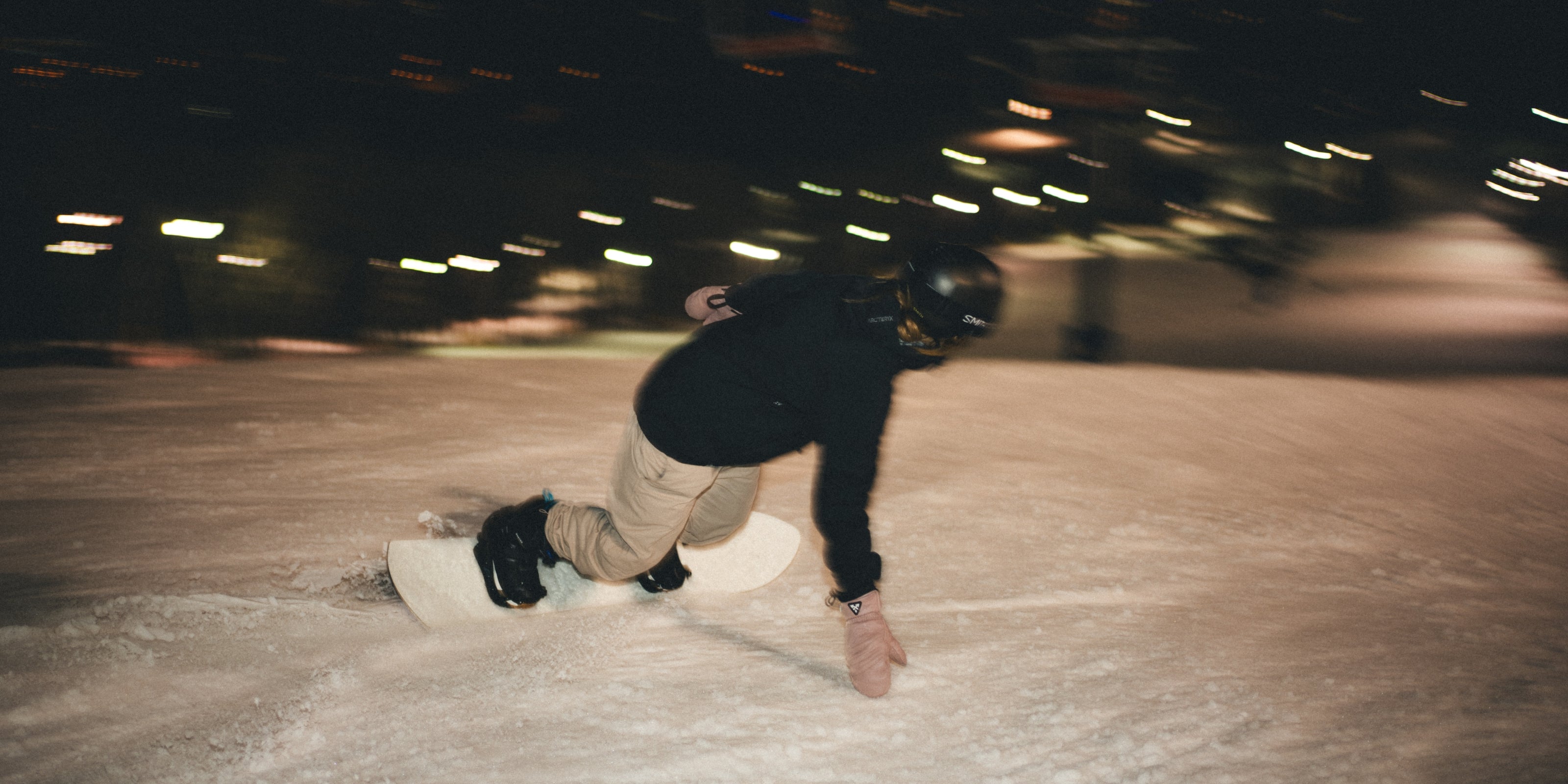 Snowboarder performing a sharp turn on a snowy slope under night lights, featuring Auclair's Powgirl glove collection